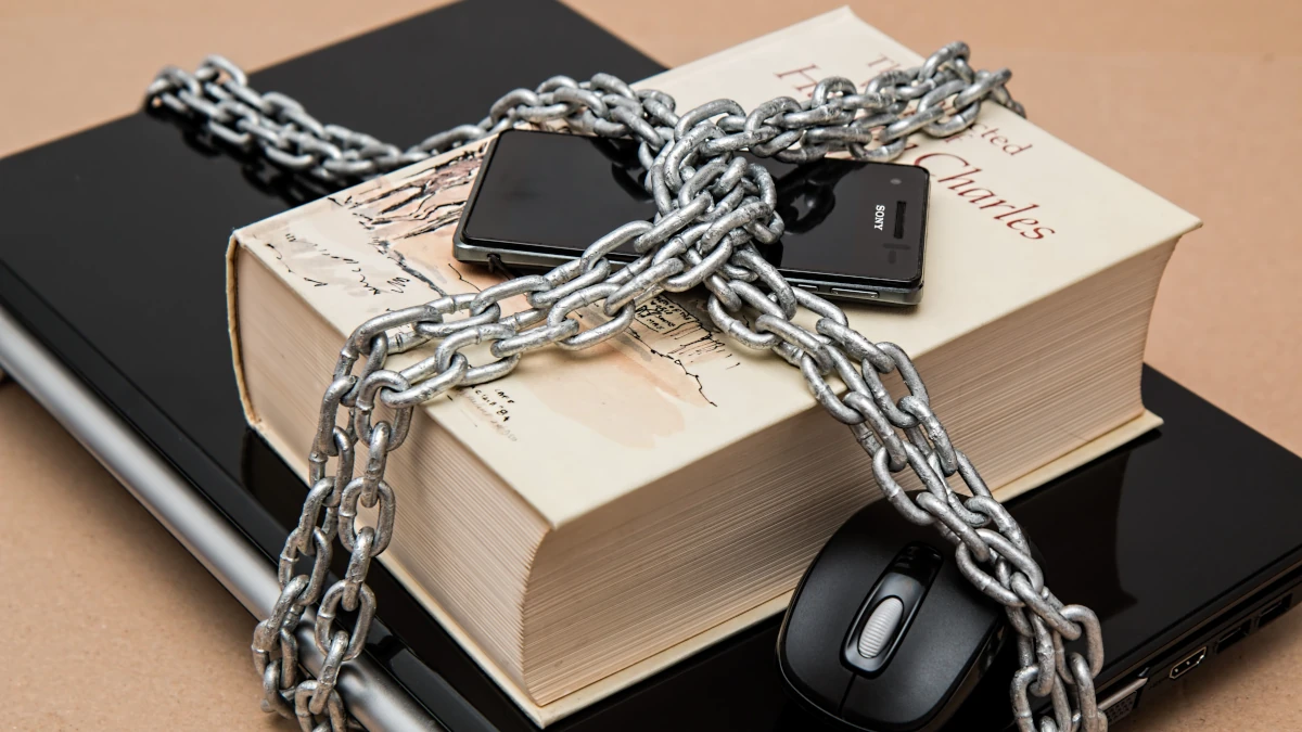 Un livre, un ordinateur portable et un smartphone fermement enchaînés, symbolisant la protection absolue et la confidentialité des manuscrits face à l'IA Cloud